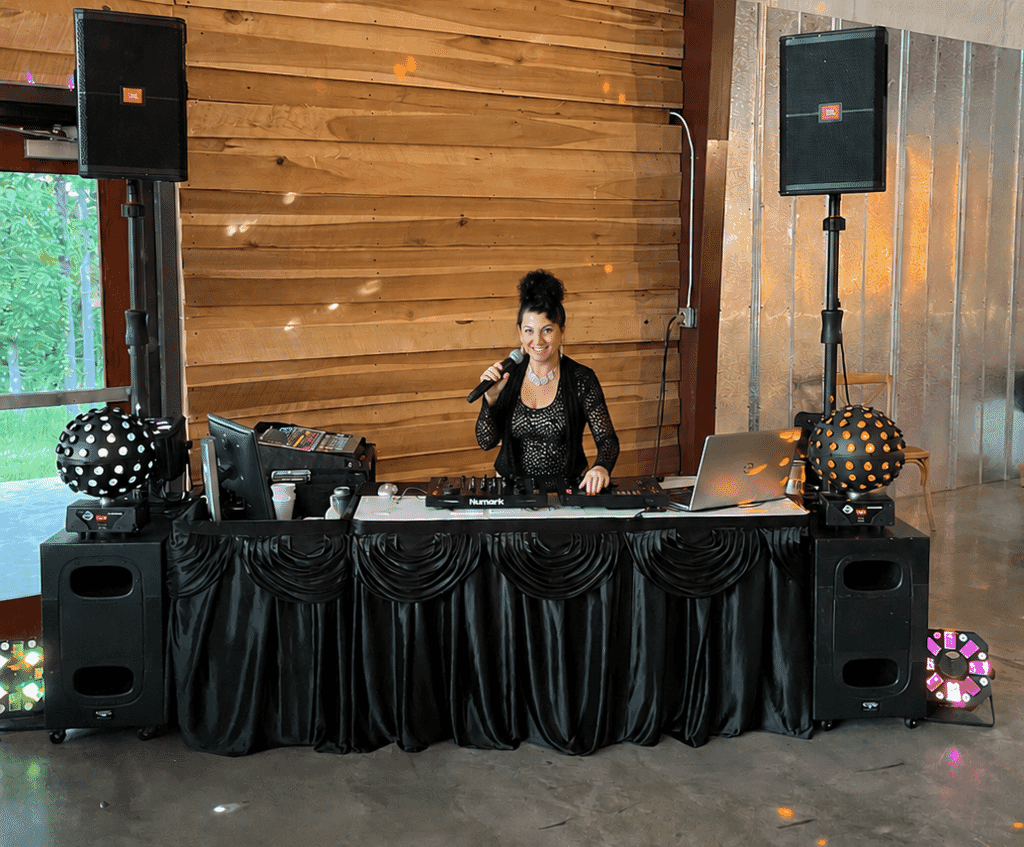 Burdoc Farms Wedding DJ | Crofton KY Wedding DJ & MC 18 Smiling female DJ holding a microphone behind a professional DJ booth with speakers and lighting.
