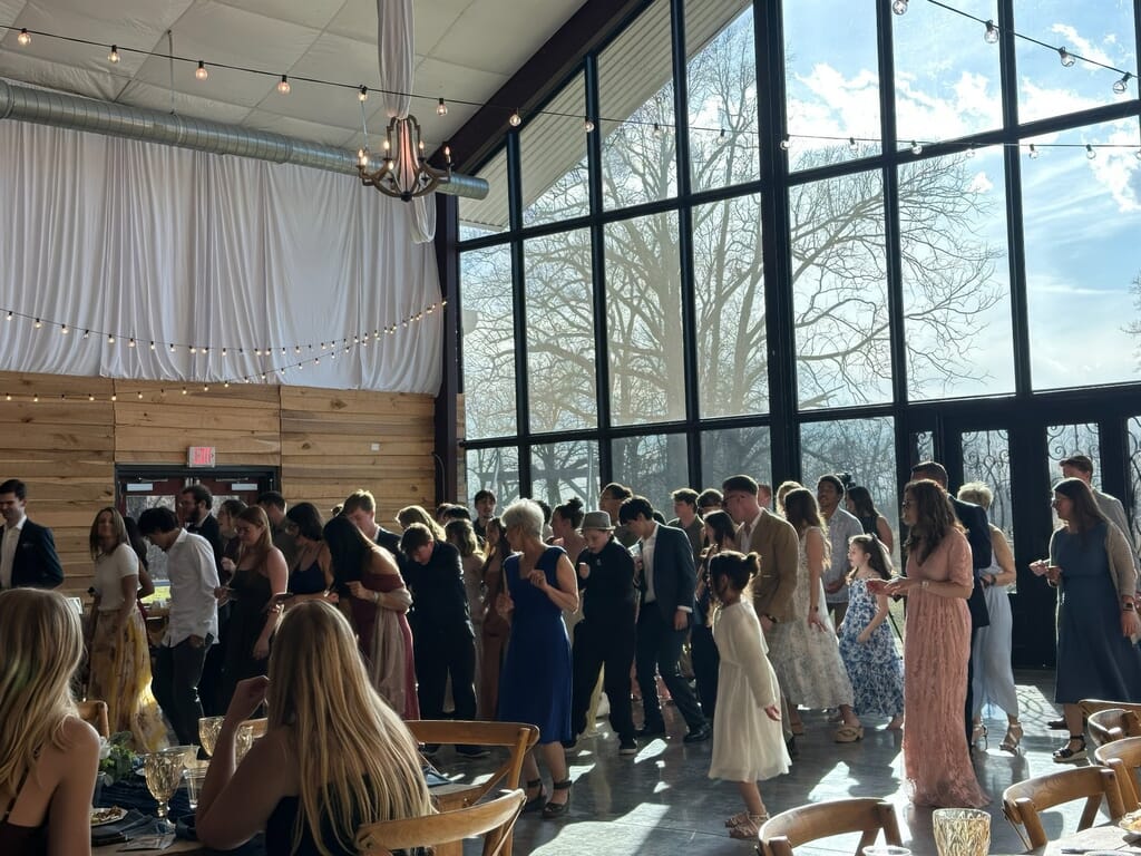 Burdoc Farms Wedding DJ | Crofton KY Wedding DJ & MC 15 Guests in semi-formal attire socialize in a bright room with floor-to-ceiling windows and wooden walls