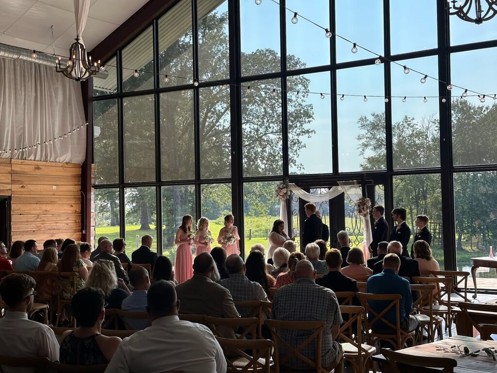 Burdoc Farms Wedding DJ | Crofton KY Wedding DJ & MC 12 Wedding ceremony in a sunlit room with floor-to-ceiling windows, featuring a bridal party at the altar and seated guests
