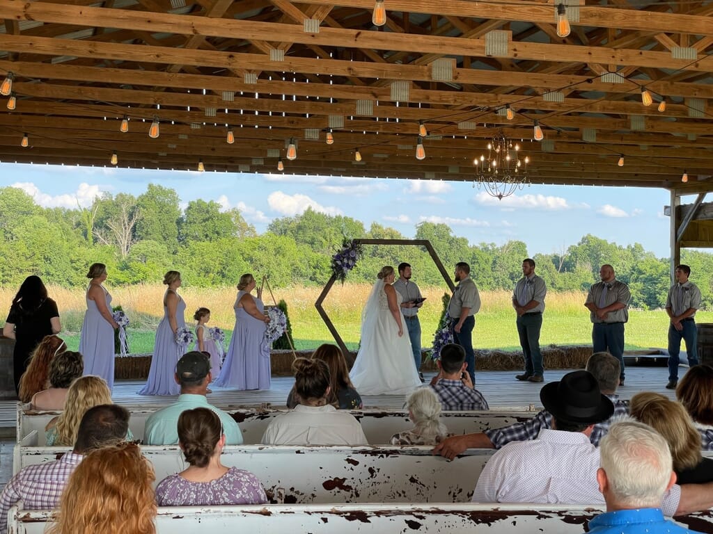 Burdoc Farms Wedding DJ | Crofton KY Wedding DJ & MC 8 A wedding ceremony under a wooden pavilion with a bride and groom standing before a hexagonal floral arch