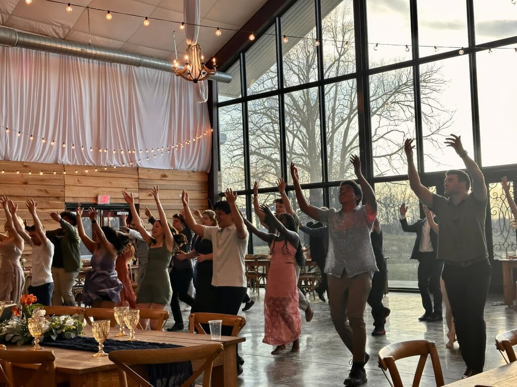 Burdoc Farms Wedding DJ | Crofton KY Wedding DJ & MC 2 Guests dancing with their arms raised in a bright event space with large windows and string lights