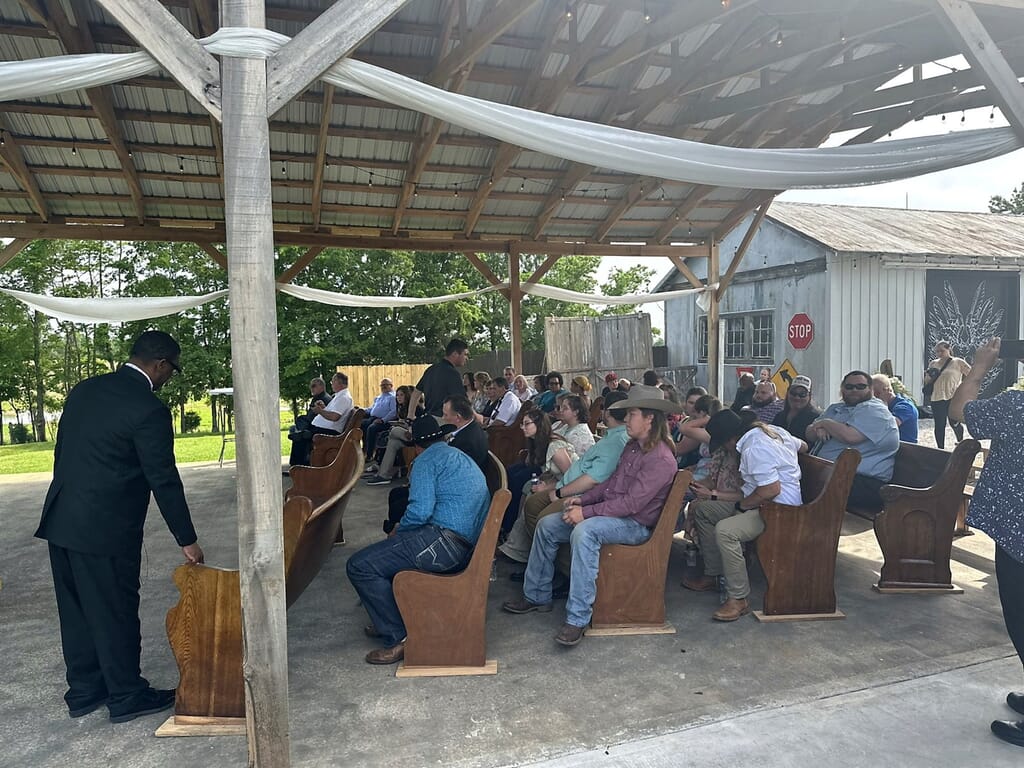 Wedding DJ Princeton Ky 8 A man in a black suit speaks from a wooden podium to a seated audience in an open-air wooden pavilion
