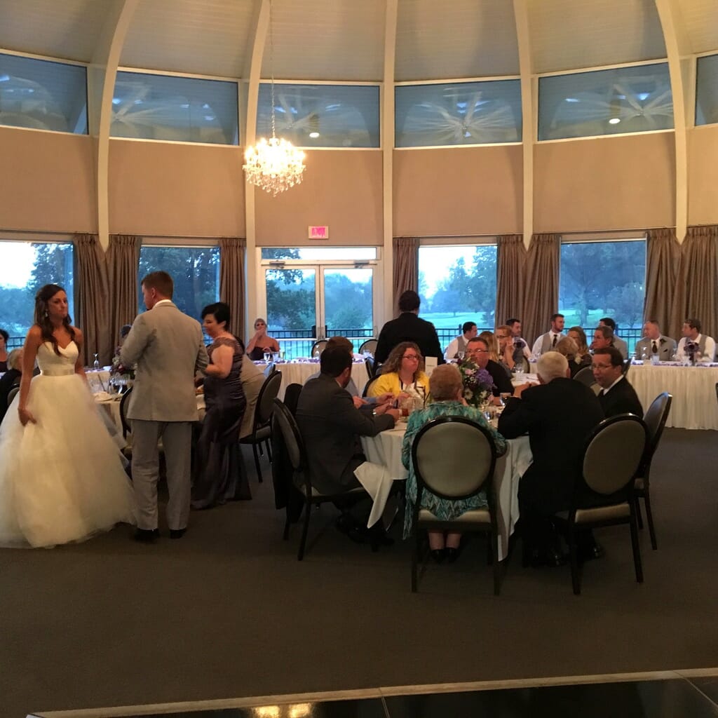 Newburgh Indiana Wedding DJ 10 A bride and groom stand near guests seated at tables in a large, bright wedding reception hall