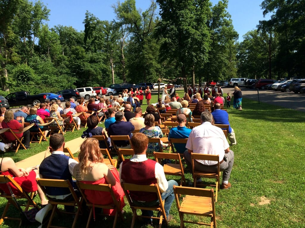 Newburgh Indiana Wedding DJ 7 Guests seated in wooden chairs on a grassy lawn for an outdoor wedding ceremony