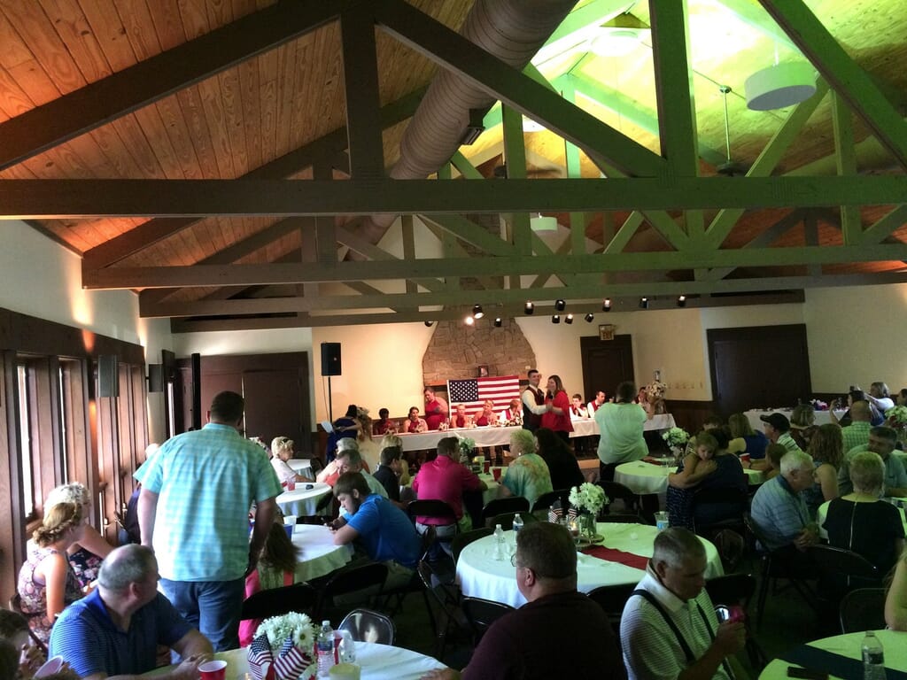 Newburgh Indiana Wedding DJ 8 Guests at round tables in a rustic hall with a high beamed ceiling, with a couple speaking at a head table