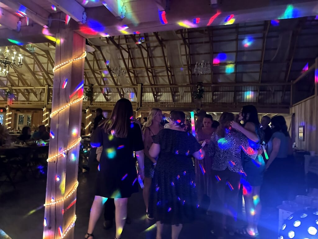 Newburgh Indiana Wedding DJ 6 People dancing in a rustic barn illuminated by colorful disco lights and warm string lights