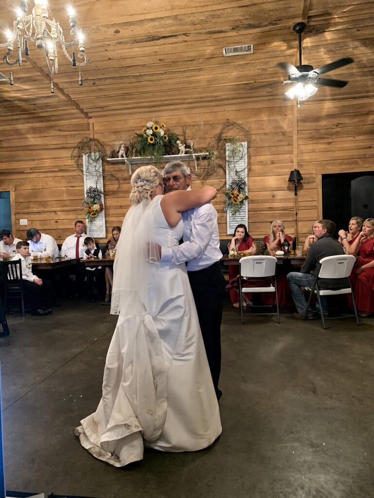 Wedding DJ Princeton Ky 17 Bride in a white wedding dress hugging a man in a rustic wood-paneled room with guests watching