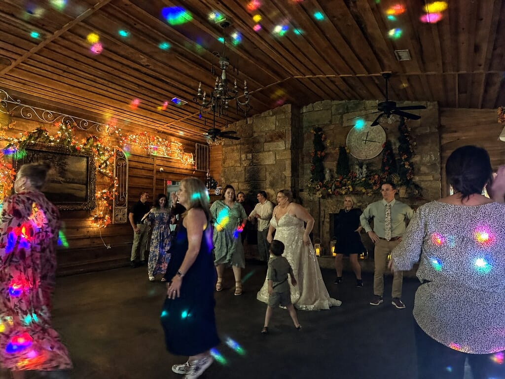 Wedding DJ Princeton Ky 16 Guests and a bride in a white gown dance in a rustic room illuminated by colorful disco lights